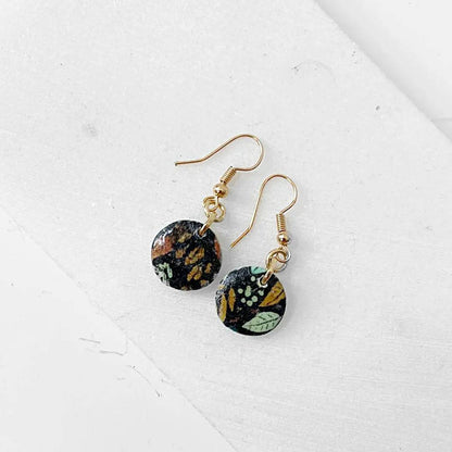 Black round polymer clay earrings with colorful leaf pattern and gold hooks. Unique and affordable accessory.