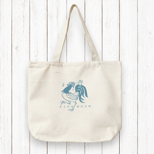 Organic canvas tote bag for singers featuring a blue hand-drawn rooster with musical notes and 'sing more' text. Eco-friendly and artist-designed.