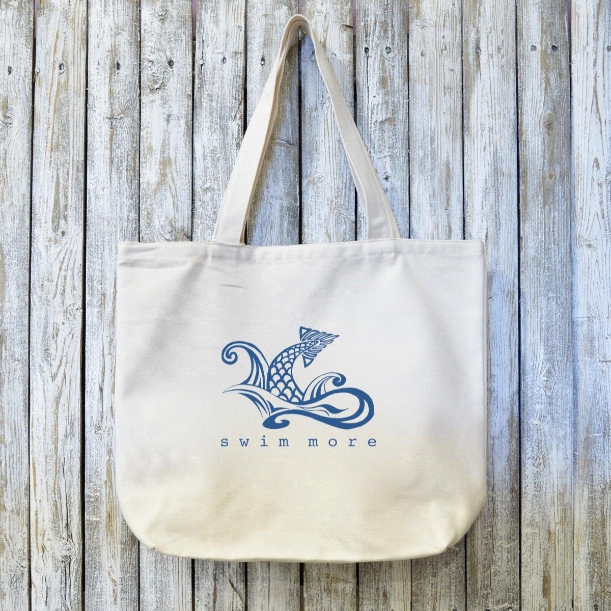 Swimmers Gift Canvas Tote with 'Swim More' fish wave design in blue ink on organic cotton. Eco-friendly tote ideal for swim gear or beach days.