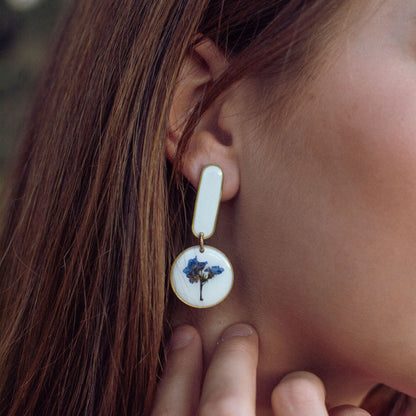 Model wearing white Modern Artist Earrings with real blue flowers and stainless steel posts, a bold accessory for creative fashion.