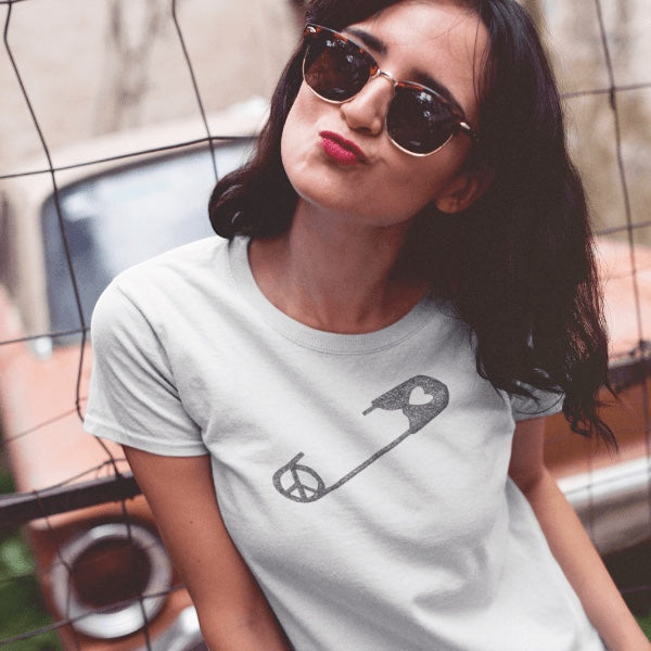 Model wearing Women's Peace & Love T-Shirt in white bamboo cotton blend with safety pin graphic. Stylish solidarity tee for advocates.