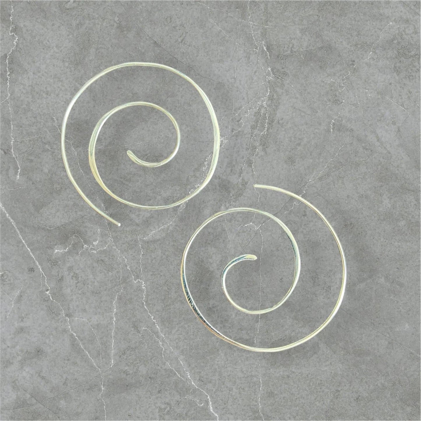 Silver Swirl Hoops - Sterling silver swirl earrings with a 1.5” diameter, displayed on a gray stone background. Elegant and minimalist jewelry design.