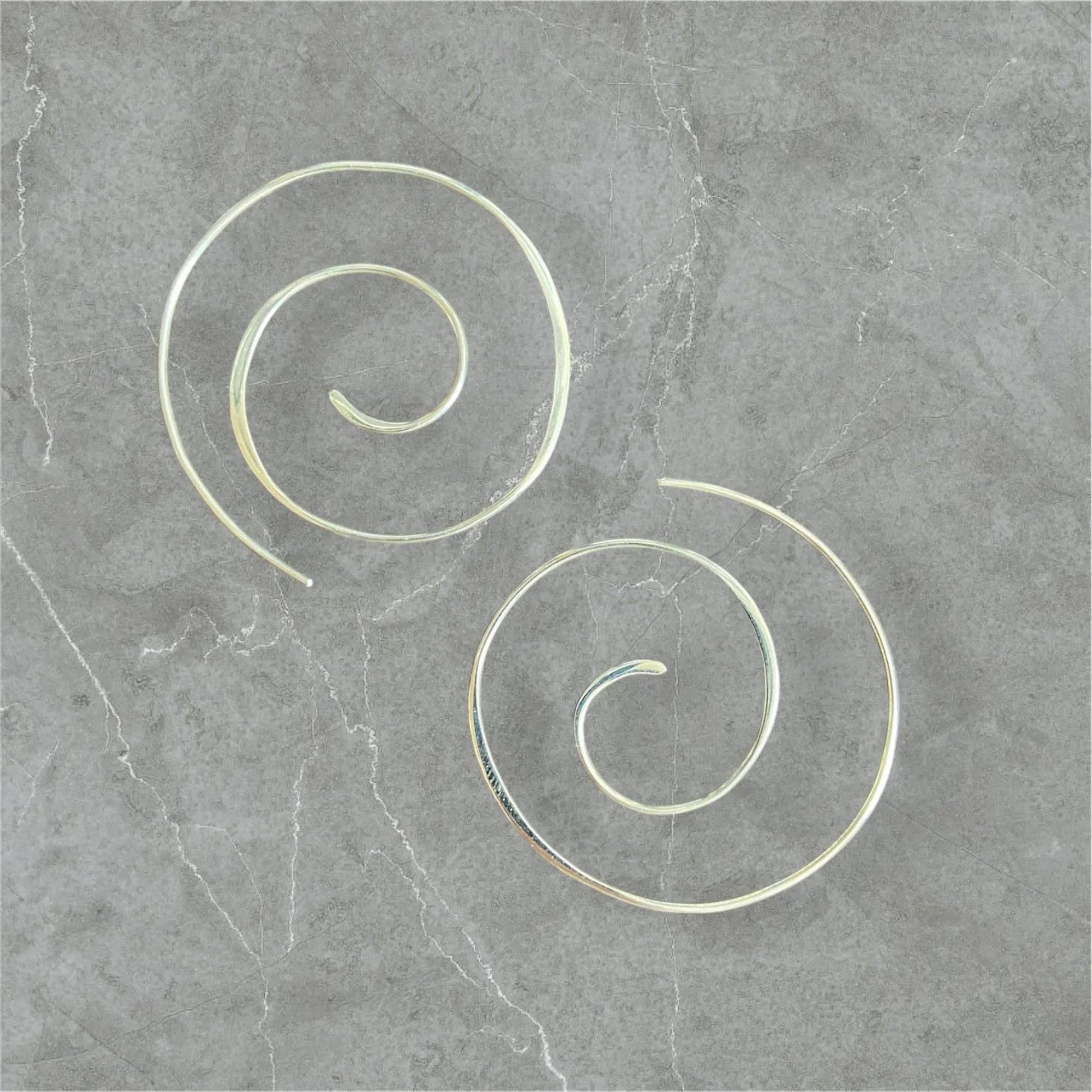 Silver Swirl Hoops - Sterling silver swirl earrings with a 1.5” diameter, displayed on a gray stone background. Elegant and minimalist jewelry design.