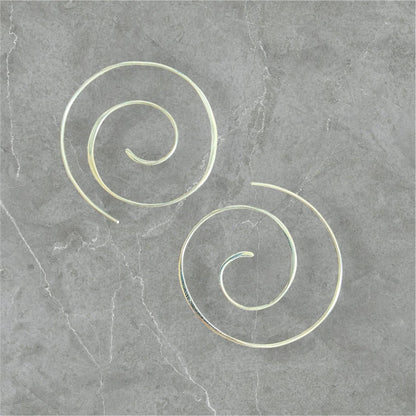 Silver Swirl Hoops - Sterling silver swirl earrings with a 1.5” diameter, displayed on a gray stone background. Elegant and minimalist jewelry design.