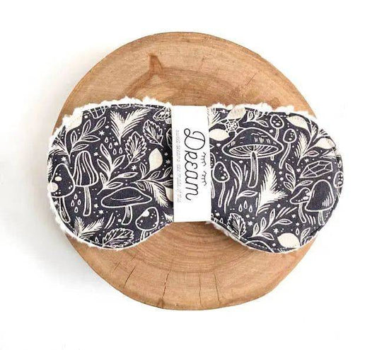 Botanical-patterned cotton sleep mask for relaxation with Sherpa lining, shown on a round wooden board. Comfortable 12-inch band included.
