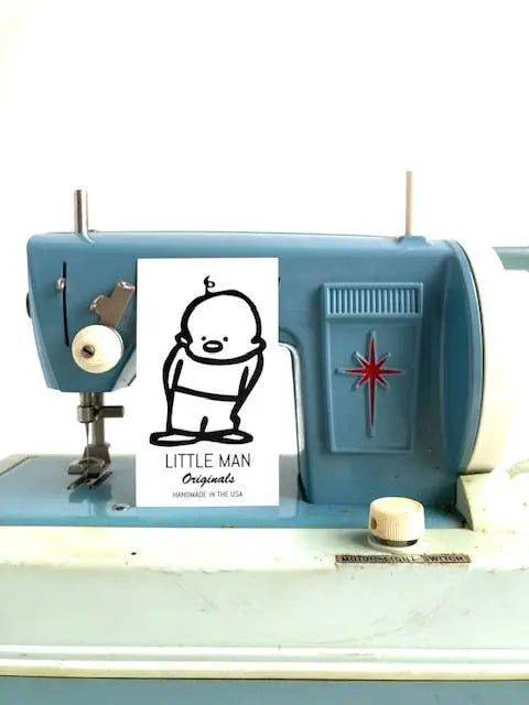 Little Man Originals logo displayed on a vintage sewing machine, highlighting handmade production of cotton sleep masks for relaxation.
