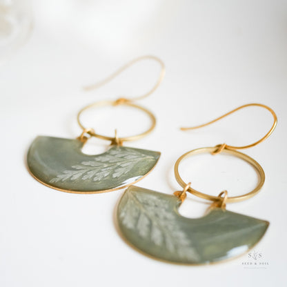 Fern Moon Shadow Earrings laid flat, showcasing semi-circle emerald resin with botanical fern detail and gold hoop, ideal for festive styling.