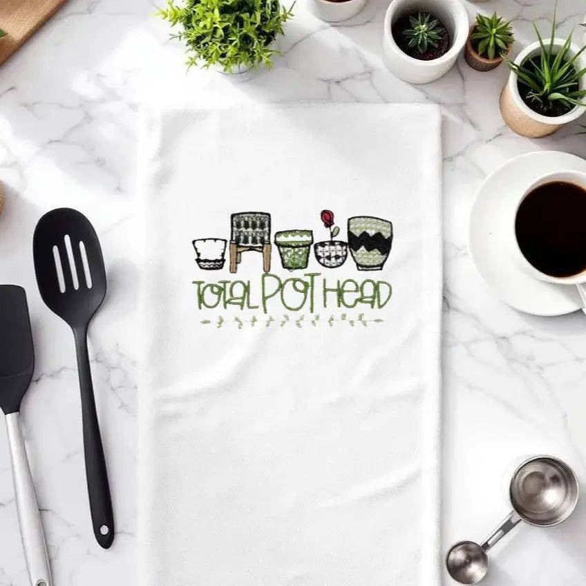 Total Pot Head Embroidered Towel - Plant-Themed Accessory displayed on a marble kitchen counter with coffee, utensils, and potted plants.
