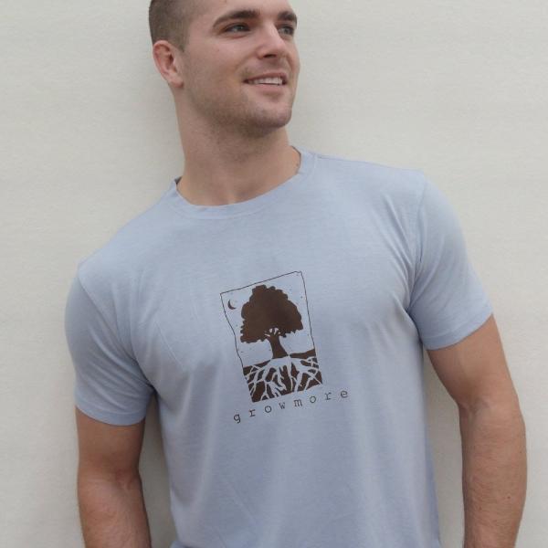 Light blue men's bamboo and organic cotton t-shirt with dark brown 'Grow More' tree and root graphic, modeled outdoors.