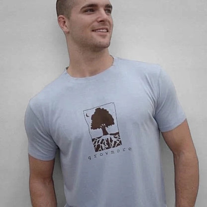 Light blue men's bamboo and organic cotton t-shirt with dark brown 'Grow More' tree and root graphic, modeled outdoors.