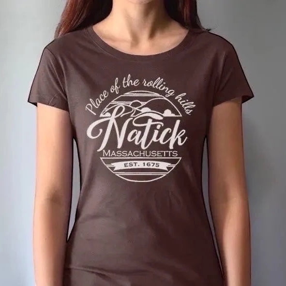 Model wearing brown women's Natick T-Shirt with 'Place of the Rolling Hills' Massachusetts graphic. Made from bamboo and organic cotton for sustainable comfort.