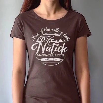 Model wearing brown women's Natick T-Shirt with 'Place of the Rolling Hills' Massachusetts graphic. Made from bamboo and organic cotton for sustainable comfort.
