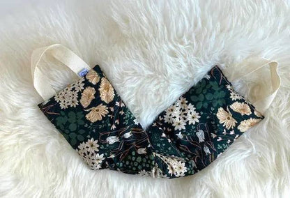 Natural pain relief wrap laid flat on white fur surface, showcasing floral cotton design and handles for easy use on neck and back.