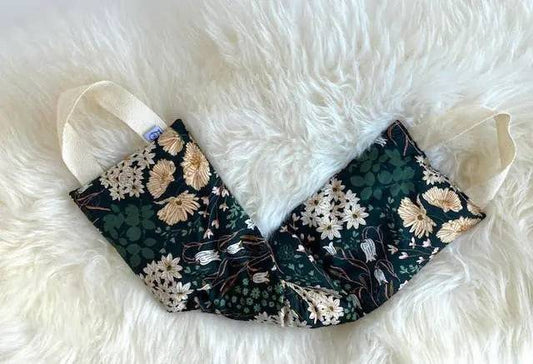 Natural pain relief wrap laid flat on white fur surface, showcasing floral cotton design and handles for easy use on neck and back.