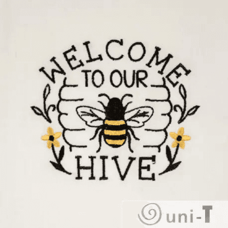 Close-up of bee embroidery with 'Welcome to Our Hive' text and yellow flowers on soft white fabric. Decorative and functional kitchen towel.