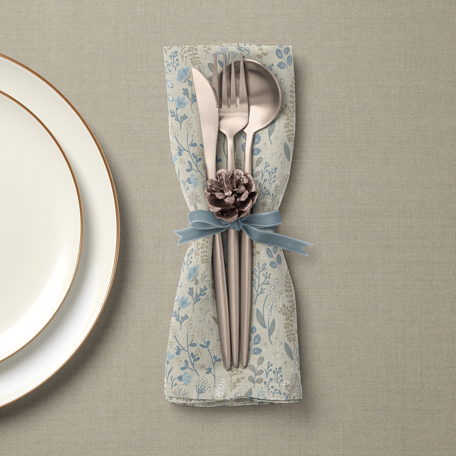 Set of linen napkins with blue floral pattern and silverware tied with blue ribbon and pinecone