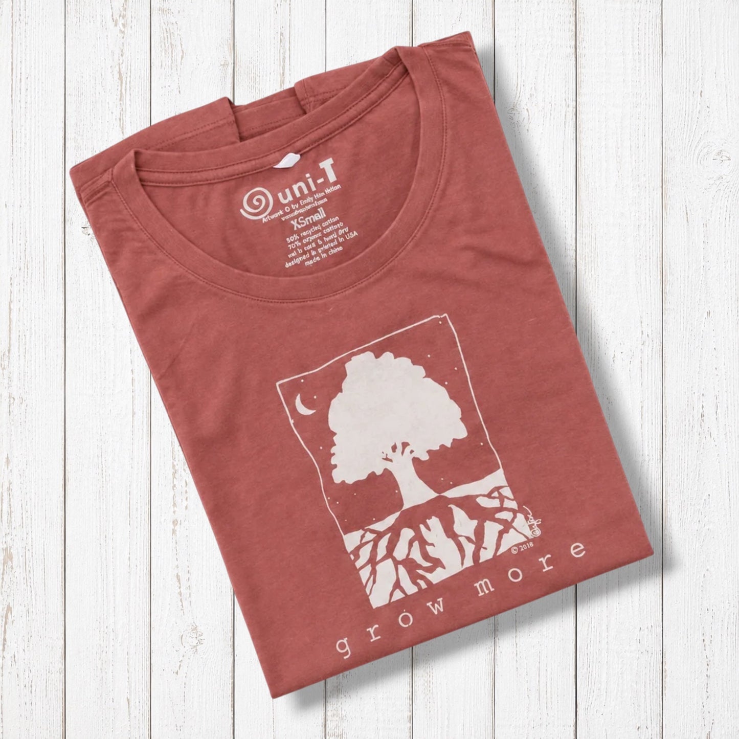 Rust-colored women's graphic T-shirt with white tree and moon design, made from organic cotton and bamboo, laid on white wooden background