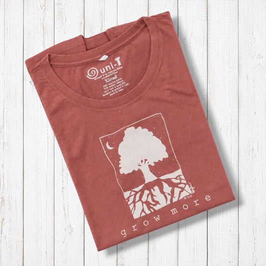 Rust-colored women's graphic T-shirt with white tree and moon design, made from organic cotton and bamboo, laid on white wooden background