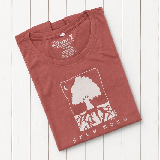 Rust-colored women's graphic T-shirt with white tree and moon design, made from organic cotton and bamboo, laid on white wooden background