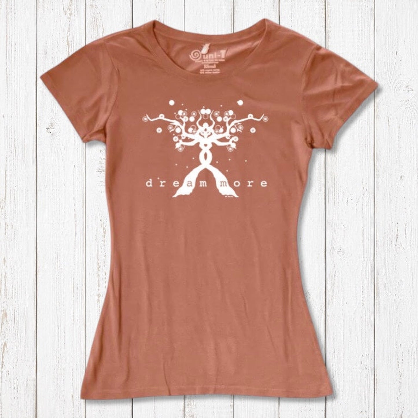 Rust-colored Women's Motivational T-Shirt in Bamboo & Organic Cotton with white 'Dream More' tree graphic, laid flat on wood background.