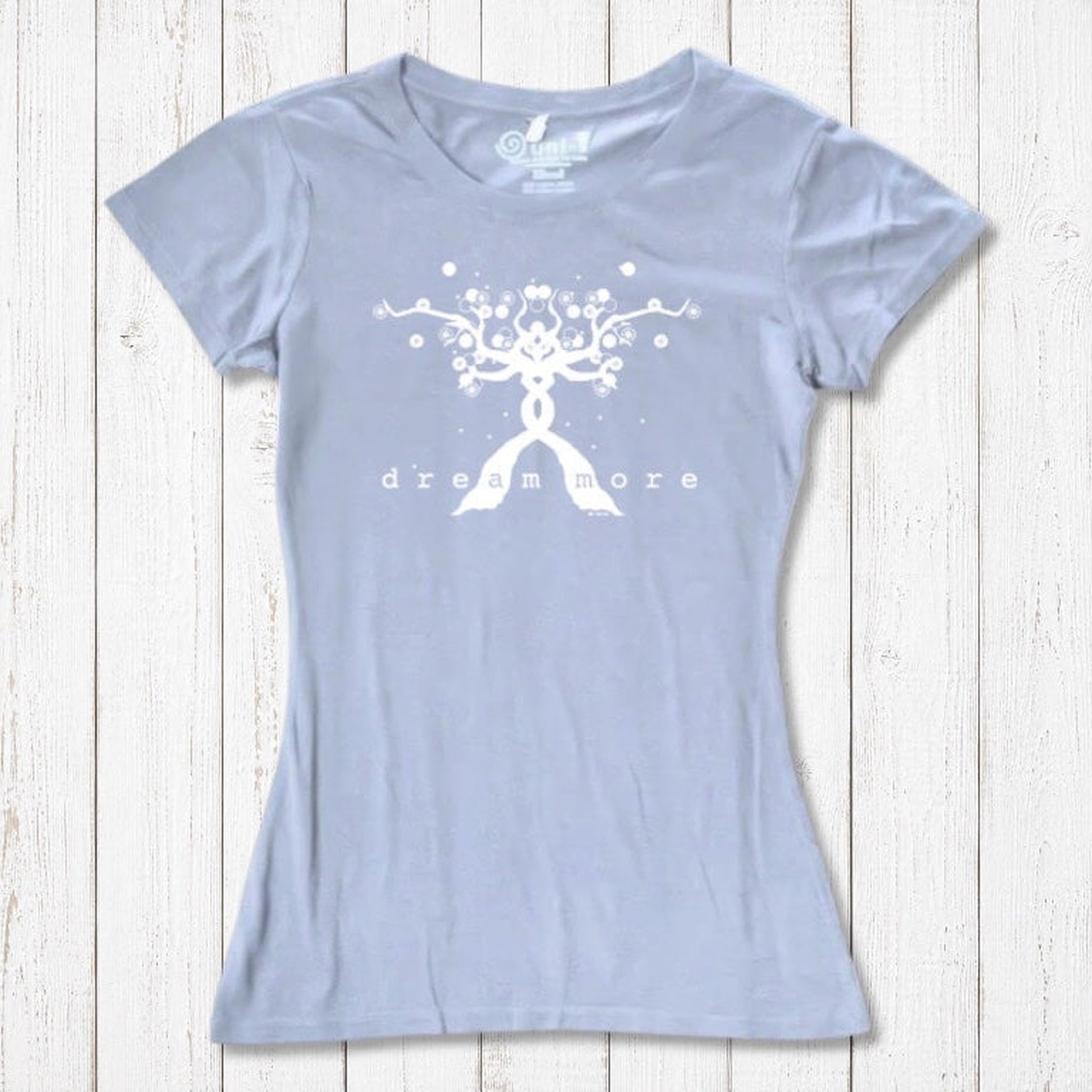 Light blue Women's Motivational T-Shirt in Bamboo & Organic Cotton with white 'Dream More' tree design, laid flat on wooden surface.