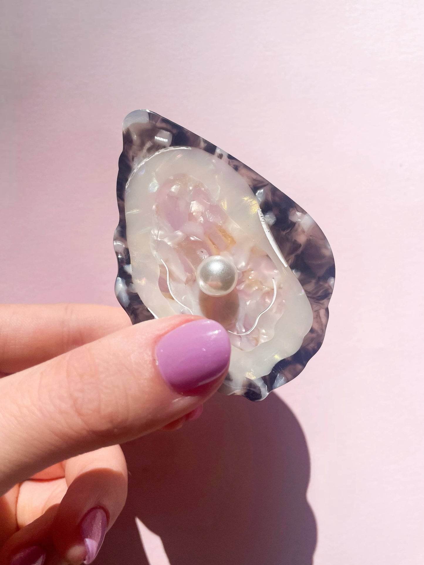 Hand holding Line&Co Oyster Claw Clip with Pearl under sunlight. Iridescent finish and pearl detail reflect elegant craftsmanship.