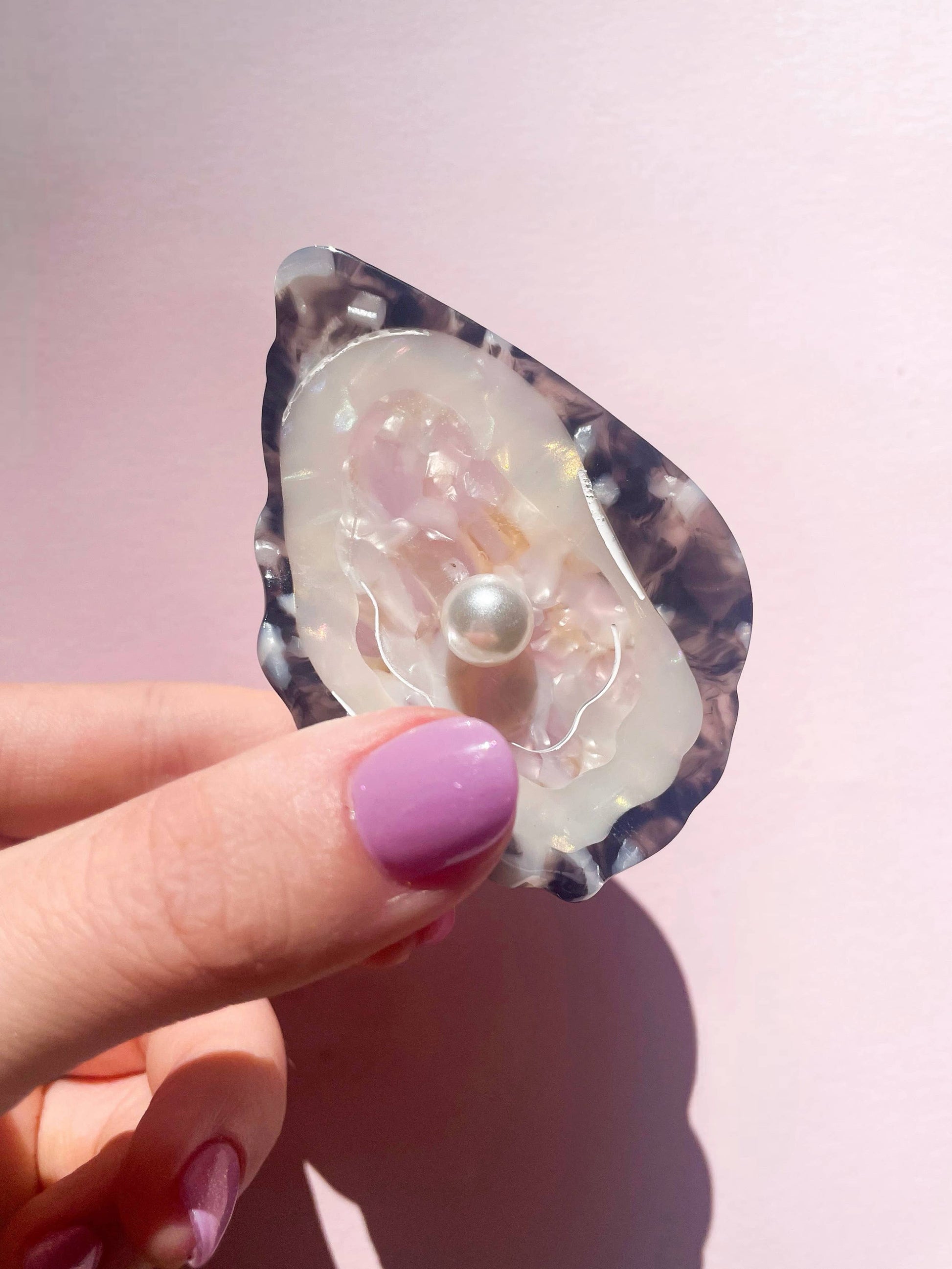 Hand holding Line&Co Oyster Claw Clip with Pearl under sunlight. Iridescent finish and pearl detail reflect elegant craftsmanship.