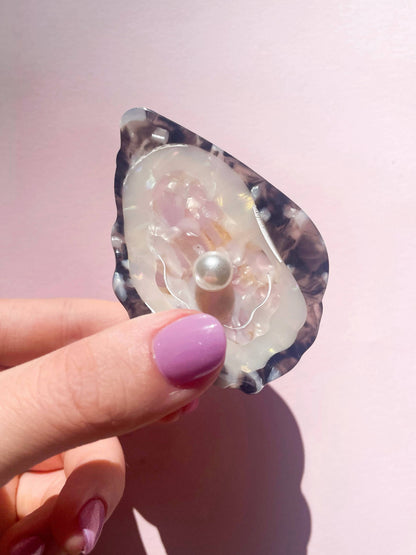 Hand holding Line&Co Oyster Claw Clip with Pearl under sunlight. Iridescent finish and pearl detail reflect elegant craftsmanship.