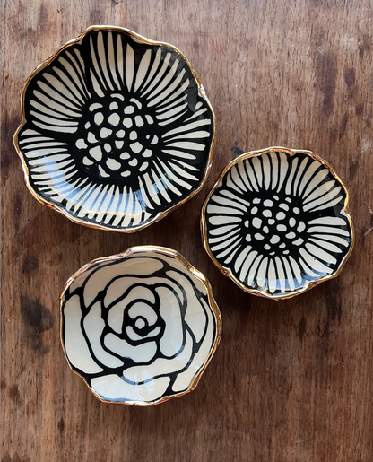 Three 4" handmade ceramic dishes with unique black floral designs and 22K gold rims, arranged on rustic wood background.