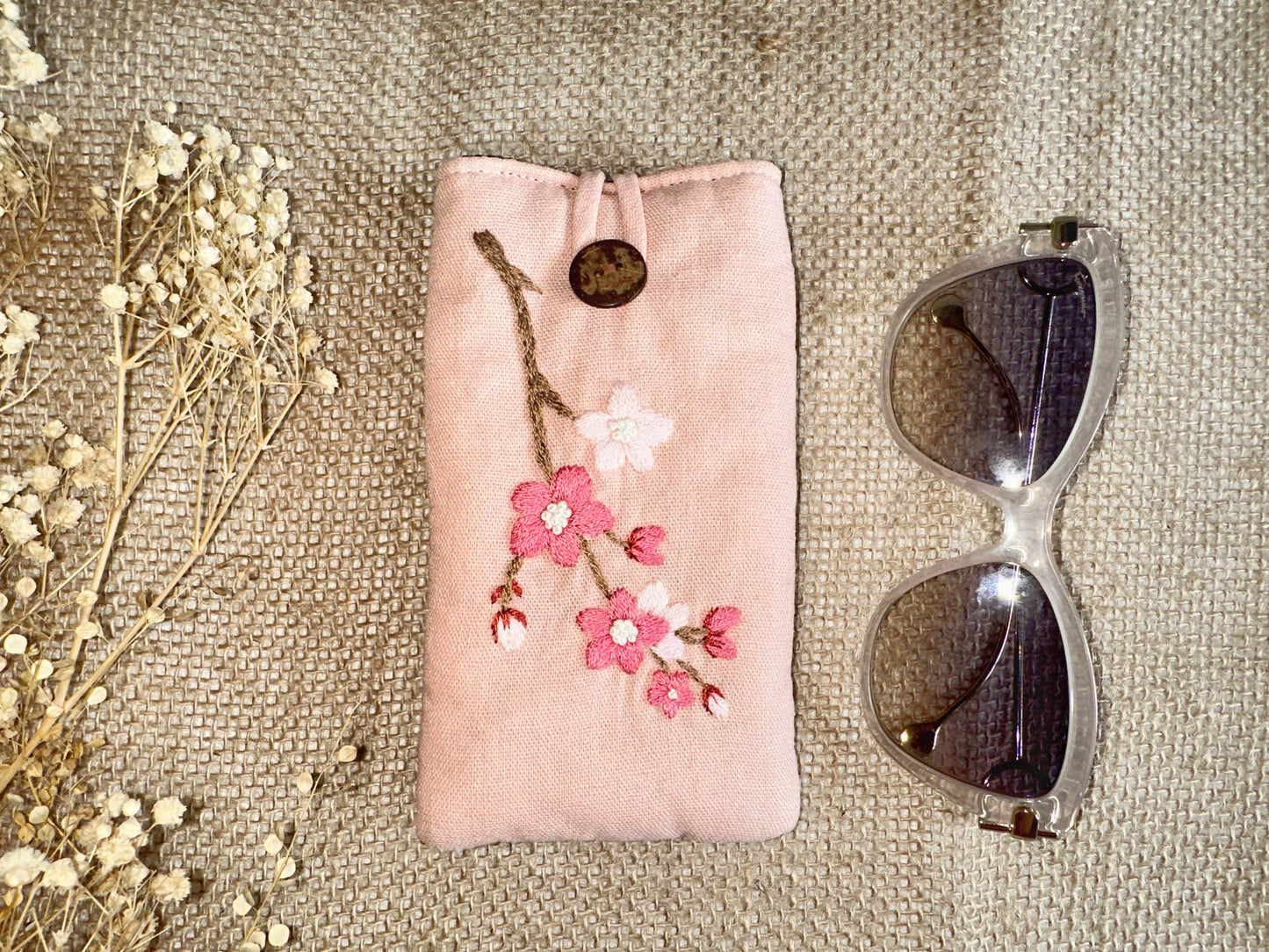 Pink linen glasses case with cherry blossom embroidery and button closure, offering padded protection for delicate eyewear.