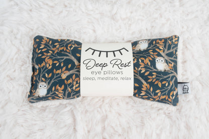 Weighted eye pillow for relaxation with owl and tree branch design, ideal for stress relief, meditation, and deep rest. Soft fabric on white fur surface.