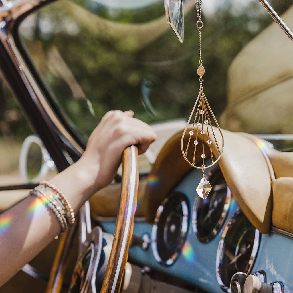 Crystal suncatcher hanging in a vintage car, casting rainbows. Elegant brass and crystal design for travel or home ambiance.