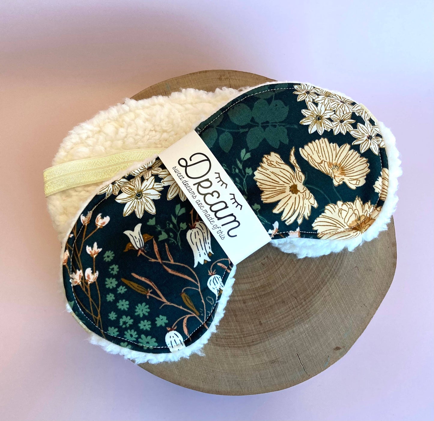 Emerald Sleep Mask with botanical design and soft fleece back, placed on a wooden tray for a cozy bedtime accessory.