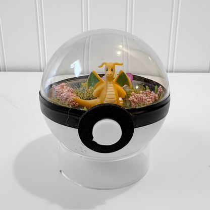 Uni-T Pokeball terrarium featuring a Dragonite figure inside a clear plastic sphere with moss and pink flowers
