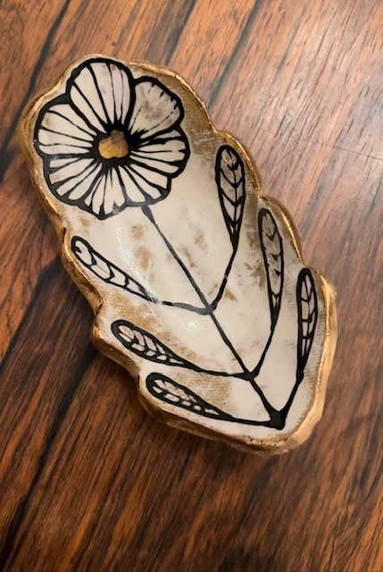 5" handmade floral shaped 22K ceramic catchall jewelry dish with abstract black floral design and gold trim, placed on wooden surface.