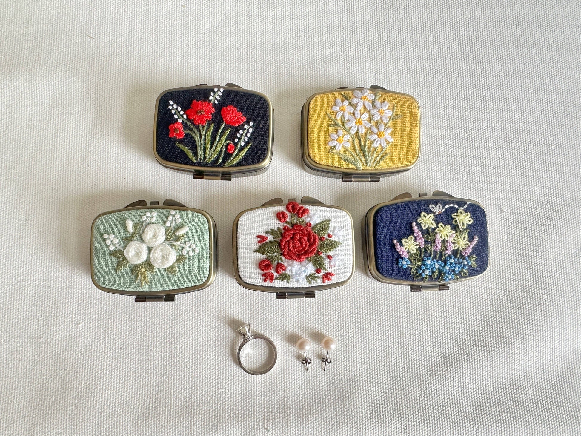Set of Five Floral Embroidered Jewelry Boxes - Elegant Storage in assorted colors and floral patterns, displayed with pearl earrings and a silver ring.
