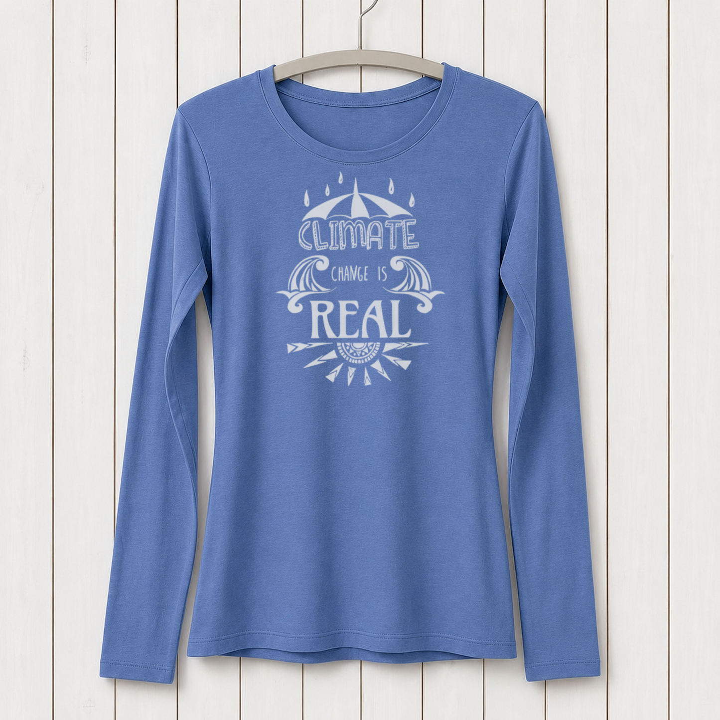 Blue long sleeve T-shirt with white graphic design featuring an umbrella, water waves, and the message 'Climate Change is Real' on a white wooden background