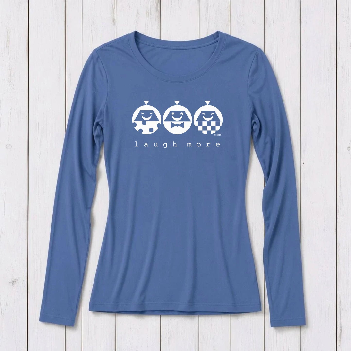 Blue long sleeve T-shirt with white graphic design featuring three smiling cartoon characters and the phrase 'laugh more' on a white wooden background