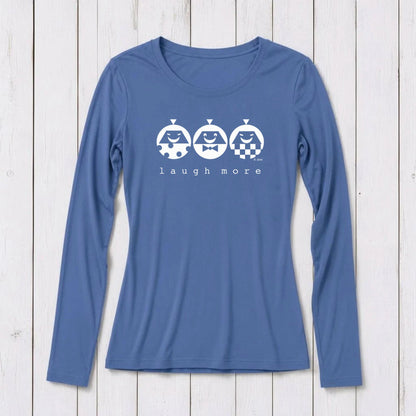 Blue long sleeve T-shirt with white graphic design featuring three smiling cartoon characters and the phrase 'laugh more' on a white wooden background