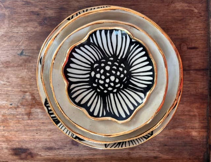 Top view of stacked 4" handmade ceramic dishes with bold black floral designs and 22K gold trim, perfect for gifting or decor.