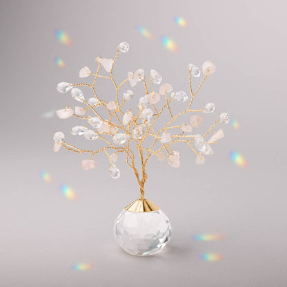 Rose Quartz Suncatcher Tree of Life with crystal and stone branches on a faceted glass base, casting rainbow reflections in soft lighting.