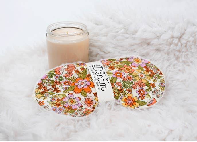 Groovy Sleep Mask with retro floral pattern placed on faux fur with a candle, showcasing cozy and relaxing bedtime ambiance.