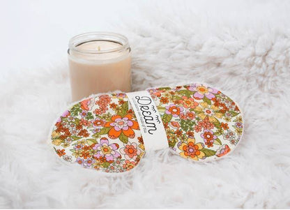 Groovy Sleep Mask with retro floral pattern placed on faux fur with a candle, showcasing cozy and relaxing bedtime ambiance.