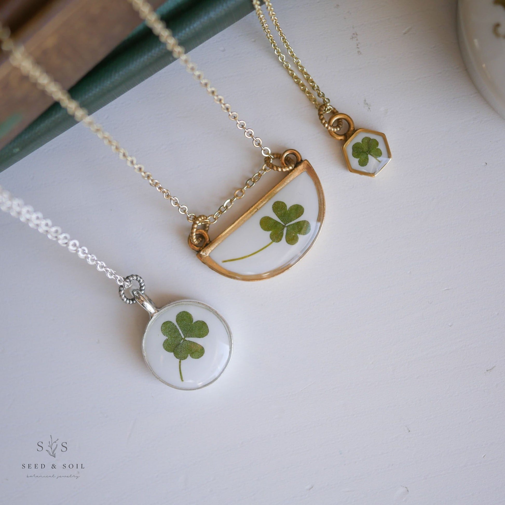 Clover pendant necklaces in hexagon, half-moon, and round styles with gold and silver chains. Symbolic jewelry for St. Patrick's Day.