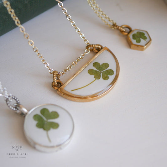 Close-up of clover necklaces in gold and silver finishes featuring real clovers in resin pendants. Ideal for celebrating luck and love.