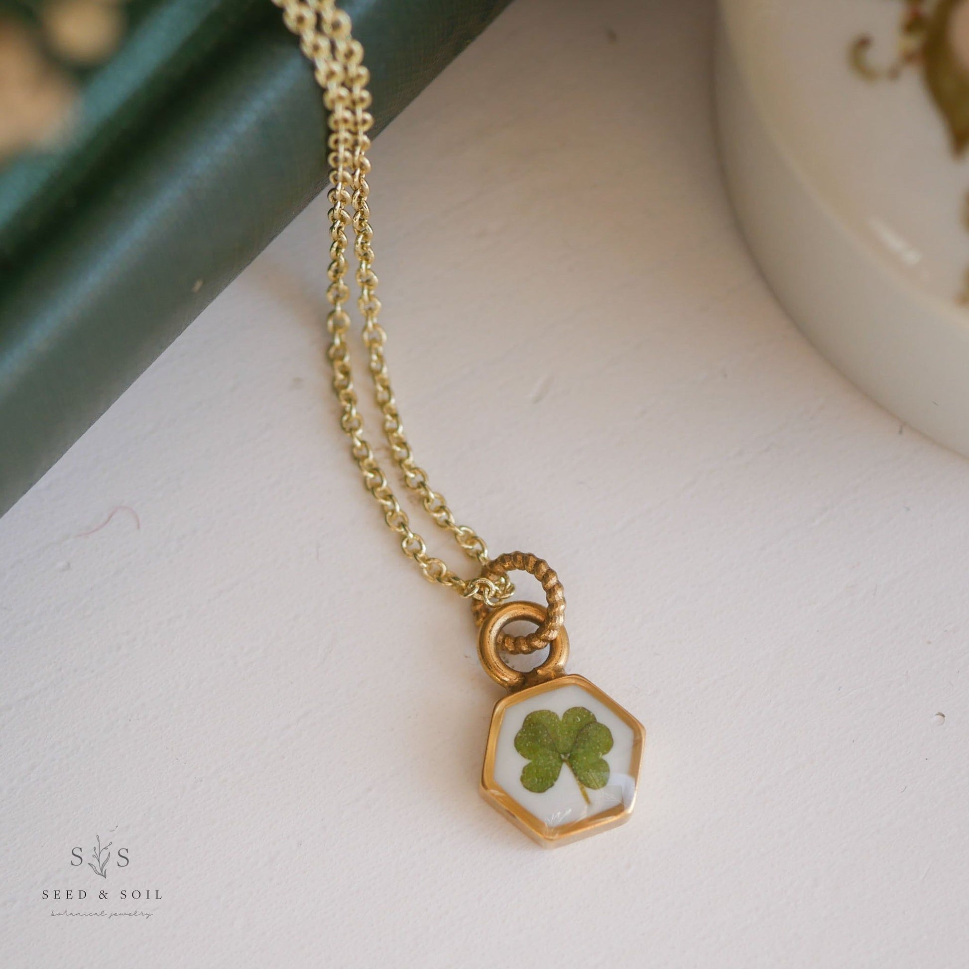 Hexagon clover pendant necklace with gold chain, showcasing a real four-leaf clover. Elegant St. Patrick's Day jewelry piece.