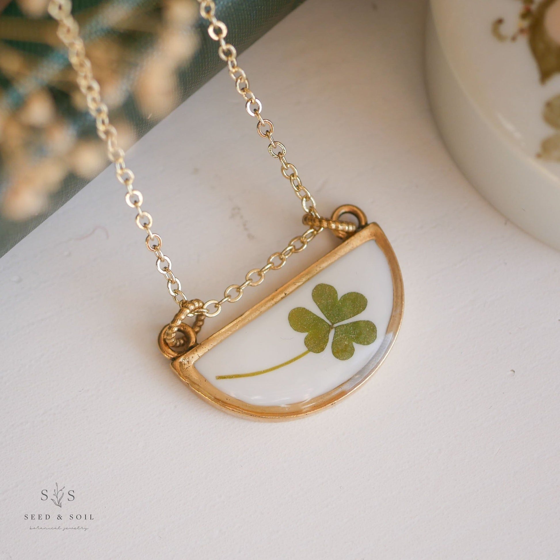 Gold half-moon clover necklace with real clover encased in resin. Unique accessory for St. Patrick’s Day celebrations.