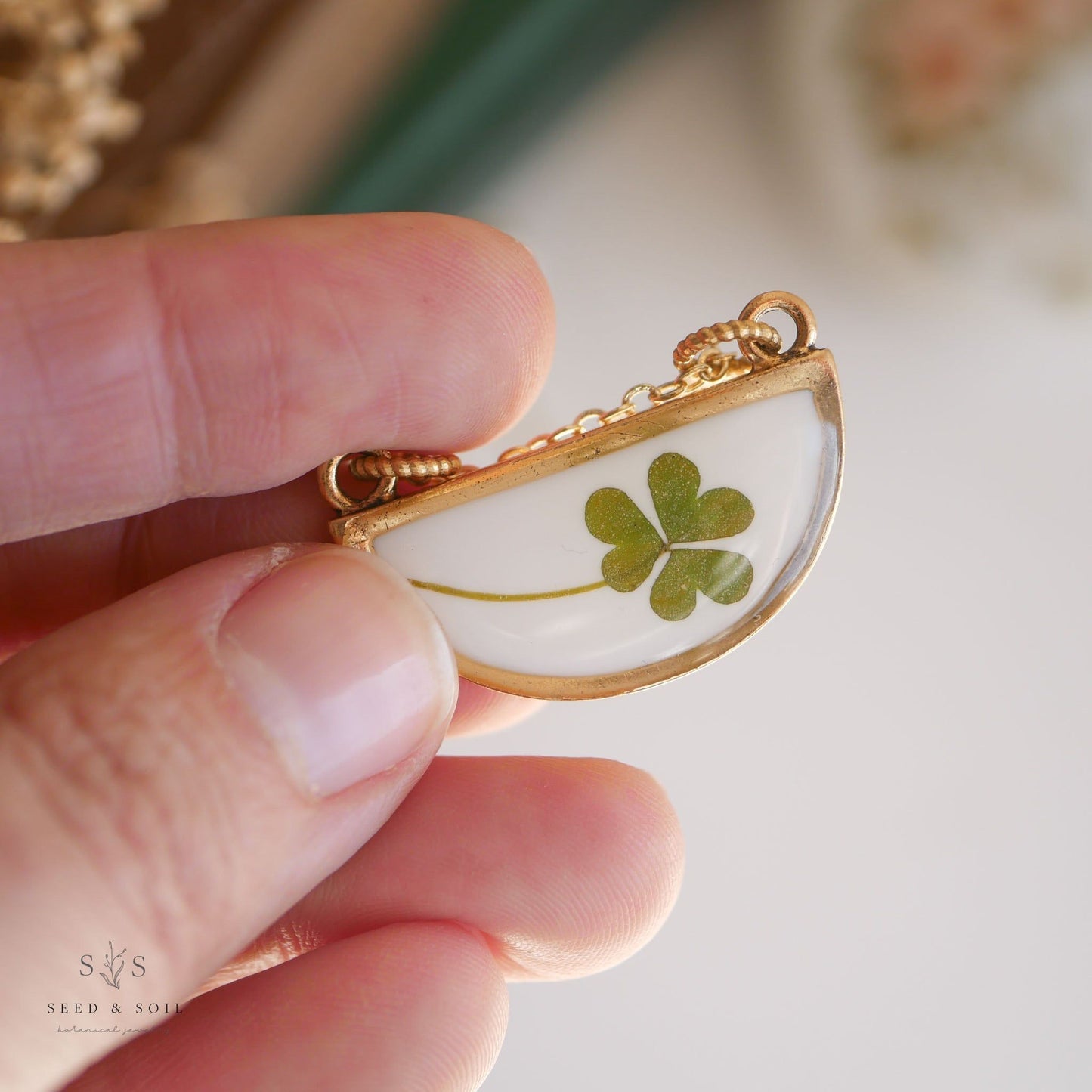 Hand holding a gold half-moon clover pendant necklace with real clover. Handmade jewelry symbolizing good fortune.