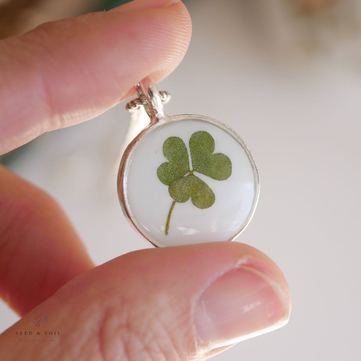 Hand holding a round silver clover pendant necklace with real clover. A meaningful gift for St. Patrick’s Day or everyday wear.