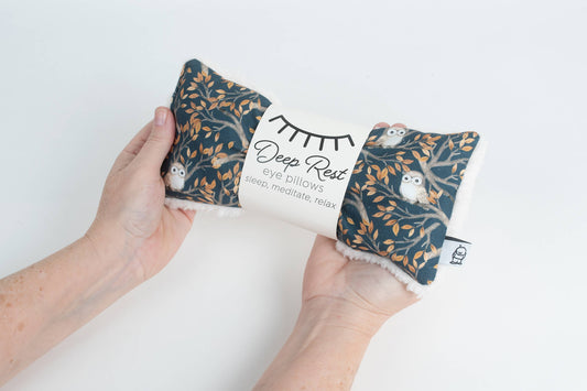 Hands holding a weighted eye pillow for relaxation featuring a night owl print, perfect for relieving stress and promoting restful sleep.